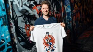 Martin Masser, ChangeNOW’s Director of Strategic Partnerships, holds a branded T-shirt in a graffiti-covered London passage.