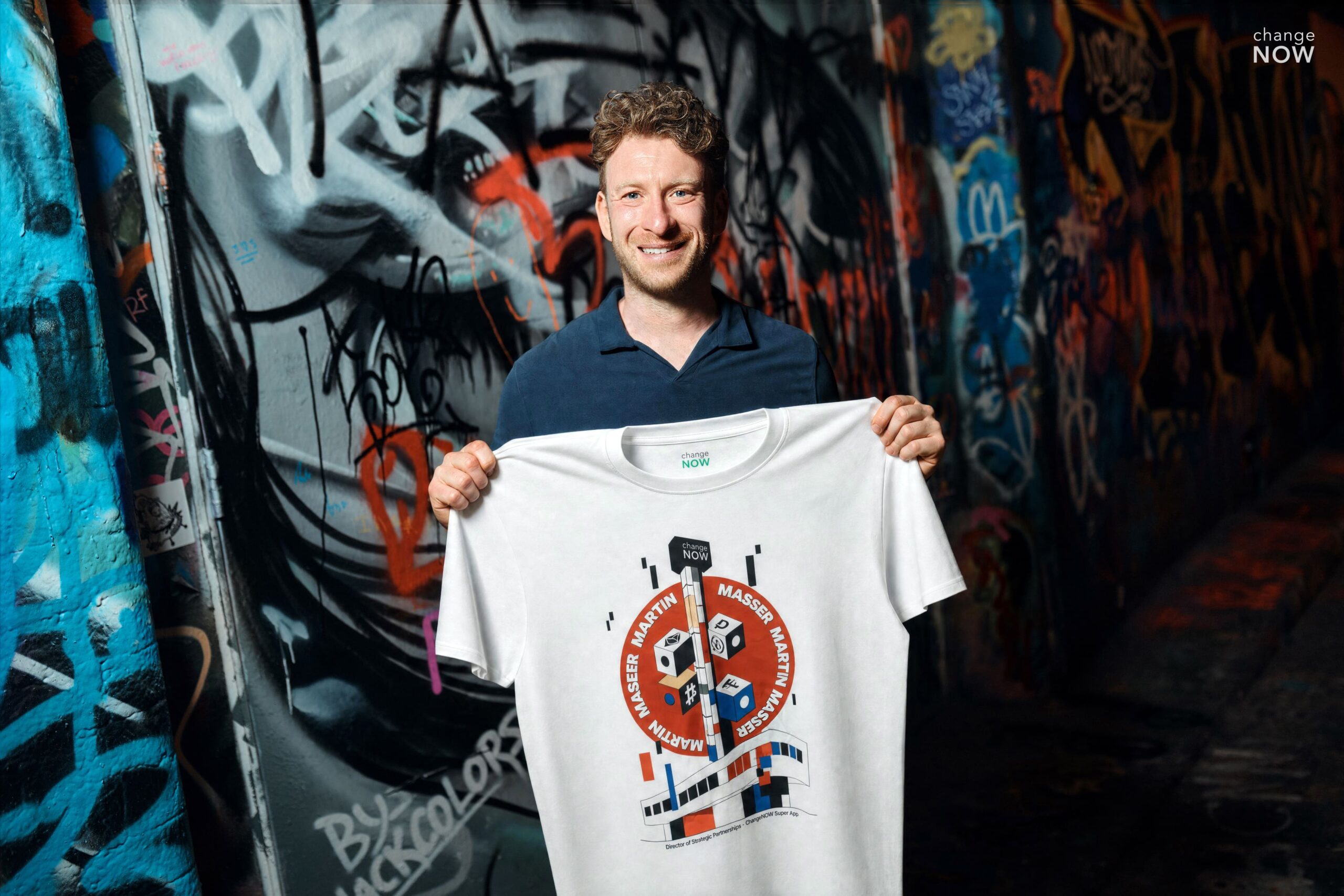 Martin Masser, ChangeNOW’s Director of Strategic Partnerships, holds a branded T-shirt in a graffiti-covered London passage.